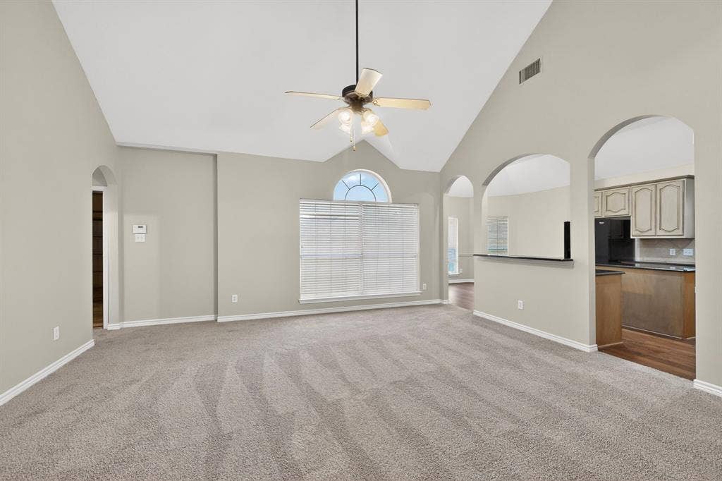 217 Gatehouse Drive, Red Oak, TX 75154 Expansive living area featuring vaulted ceilings, a ceiling fan, arched doorways, a large window with an arched transom, and plush carpeting