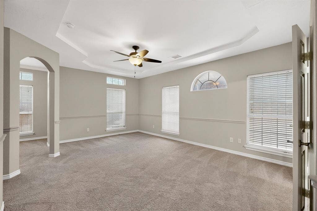 217 Gatehouse Drive, Red Oak, TX 75154 Spacious room featuring a tray ceiling with a ceiling fan, arched doorway, and multiple windows including an arched transom window