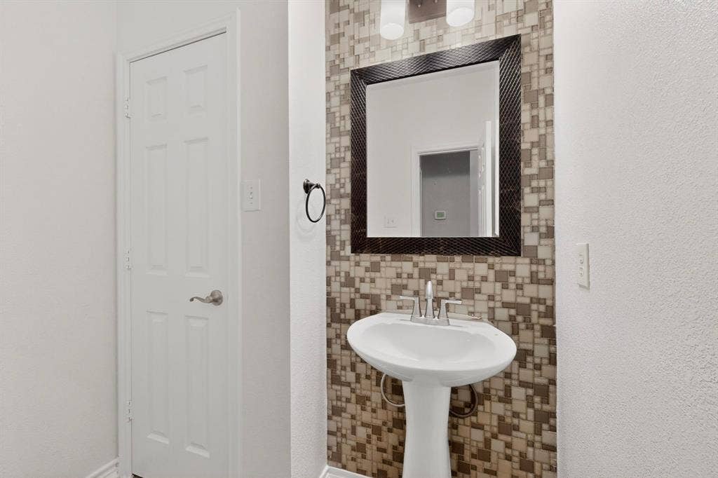 217 Gatehouse Drive, Red Oak, TX 75154 Pedestal sink with a brushed nickel faucet, framed mirror, and mosaic tile wall covering