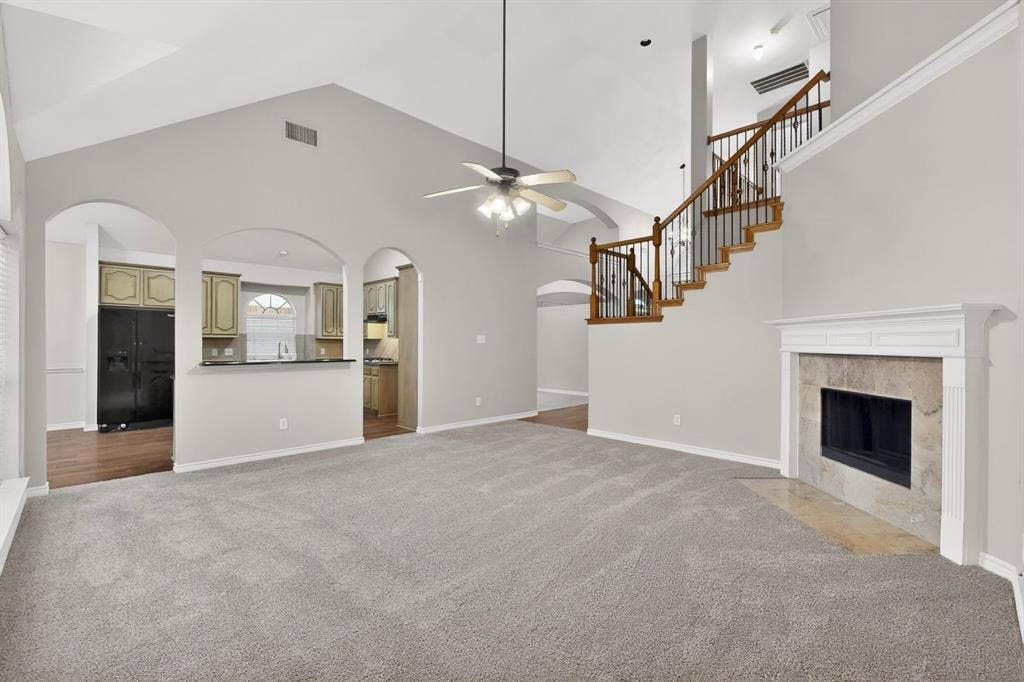 217 Gatehouse Drive, Red Oak, TX 75154 Vaulted ceiling living space featuring a fireplace with a stone surround, a wood staircase with black wrought iron balusters, and arched doorways leading to the kitchen