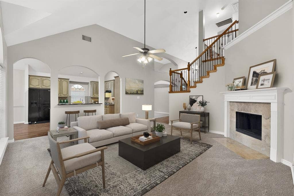 217 Gatehouse Drive, Red Oak, TX 75154 Vaulted ceiling living space featuring a fireplace with a stone surround, a wood staircase with black wrought iron balusters, and arched doorways leading to the kitchen