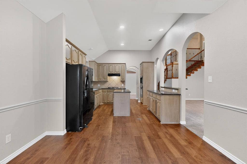 217 Gatehouse Drive, Red Oak, TX 75154 Kitchen featuring wood-finish flooring, an island with countertop, built-in cabinetry, arched doorways, and a tile backsplash