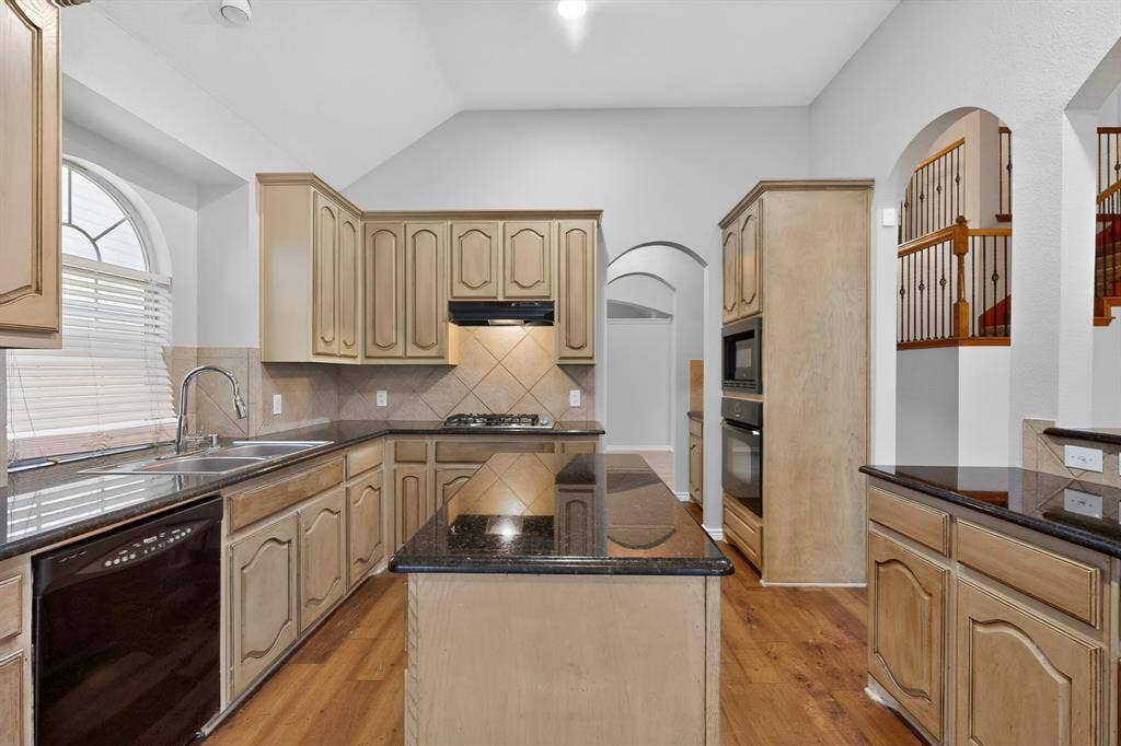 217 Gatehouse Drive, Red Oak, TX 75154 Spacious kitchen featuring light wood-finish cabinetry, black countertops, a central island, integrated appliances, and wood-finish flooring