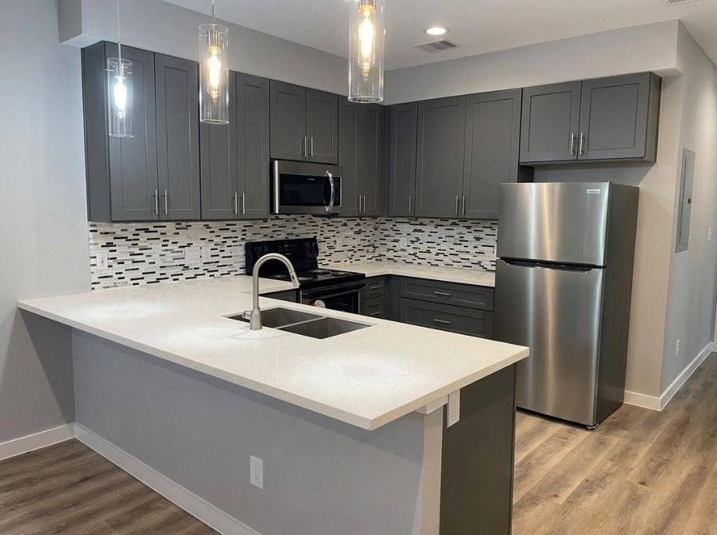 9114 Caddo Road, #A & B, Houston, TX 77078 Modern kitchen featuring a peninsula with integrated sink, stainless steel appliances, dark cabinetry, and a mosaic tile backsplash