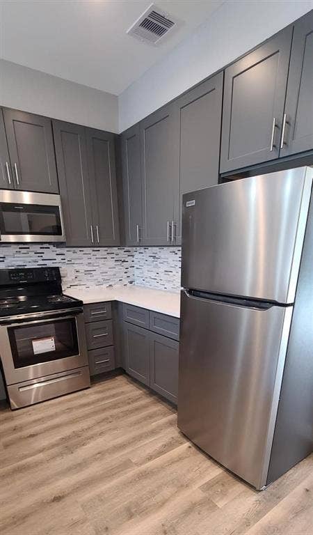 9114 Caddo Road, #A & B, Houston, TX 77078 Modern kitchen featuring gray shaker-style cabinetry, stainless steel appliances, white countertops, and a mosaic tile backsplash