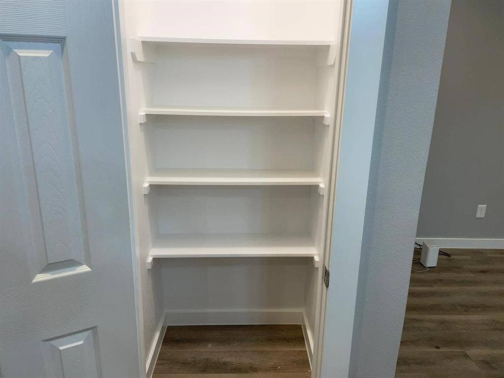 9114 Caddo Road, #A & B, Houston, TX 77078 Kitchen Pantry with Built-in shelving unit with five white shelves, white baseboard, and wood-finish flooring