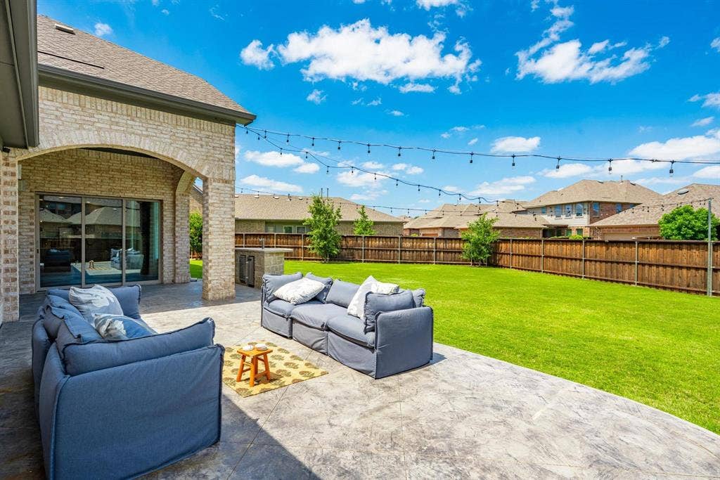 1205 Shady Fox Way, Arlington, TX 76005 Spacious concrete patio featuring an arched brick-clad covered area, built-in outdoor kitchen with stone finish, and string lighting