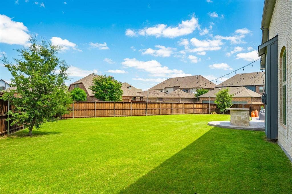 1205 Shady Fox Way, Arlington, TX 76005 Expansive green lawn framed by a privacy fence, featuring a mature tree, stone patio, and string lighting
