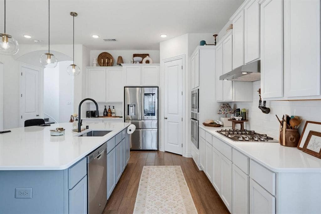 1205 Shady Fox Way, Arlington, TX 76005 Kitchen featuring a large central island with a built-in sink and dishwasher, white countertops, wood-finish flooring, white cabinetry, and stainless steel appliances