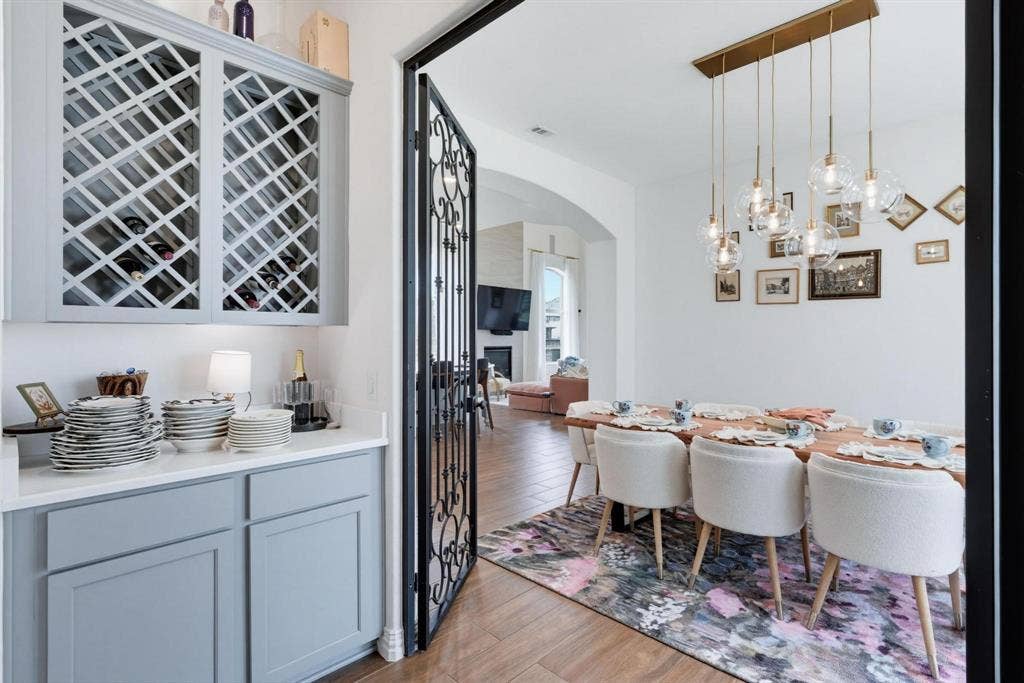 1205 Shady Fox Way, Arlington, TX 76005 Formal dining area featuring a linear chandelier with multiple glass globe pendants, wood-finish flooring, a white accent wall, and an ornate wrought-iron door