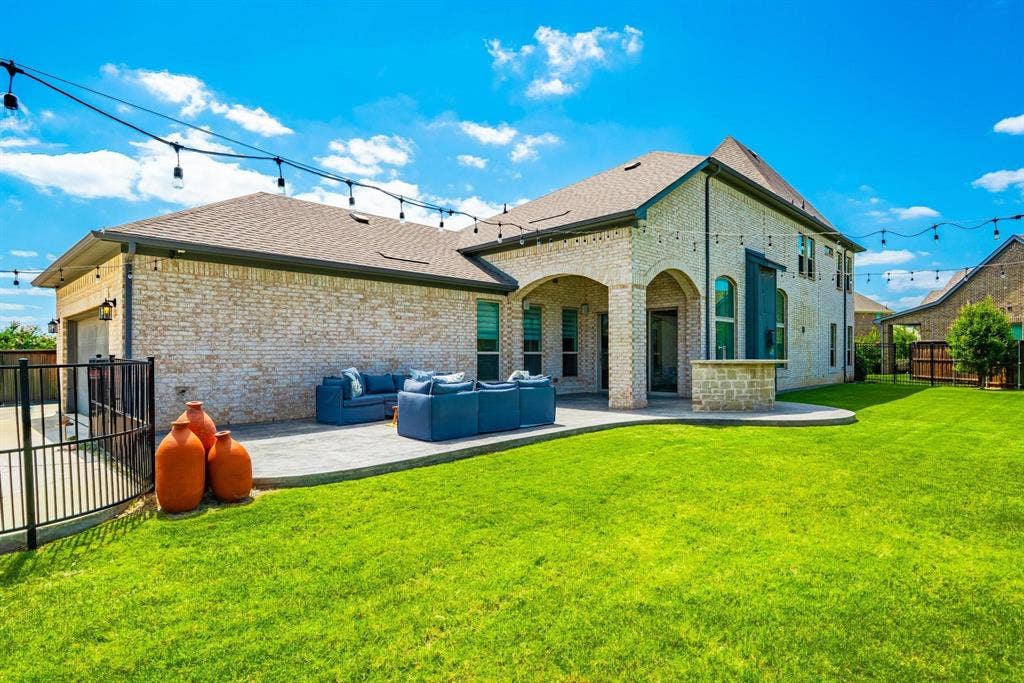1205 Shady Fox Way, Arlington, TX 76005 Expansive backyard featuring a manicured lawn, string lighting, and a brick exterior