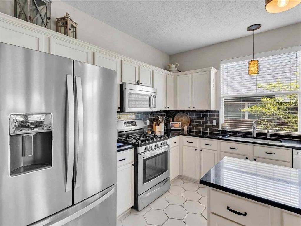 6004 Crestmill Lane, Sachse, TX 75048 Kitchen featuring stainless steel appliances, white cabinetry, dark countertops, and a subway tile backsplash