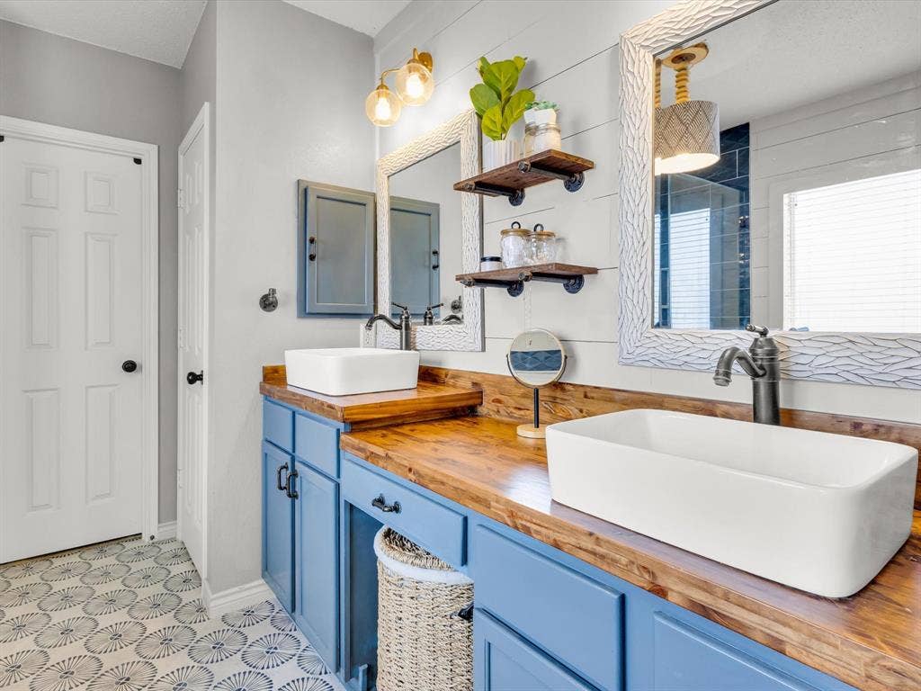 6004 Crestmill Lane, Sachse, TX 75048 Dual vessel sinks set on a wood-finish countertop with blue cabinetry