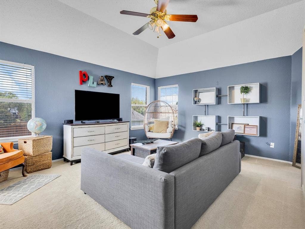 6004 Crestmill Lane, Sachse, TX 75048 Vaulted ceiling room featuring multiple windows, a ceiling fan with integrated lighting, and carpet flooring