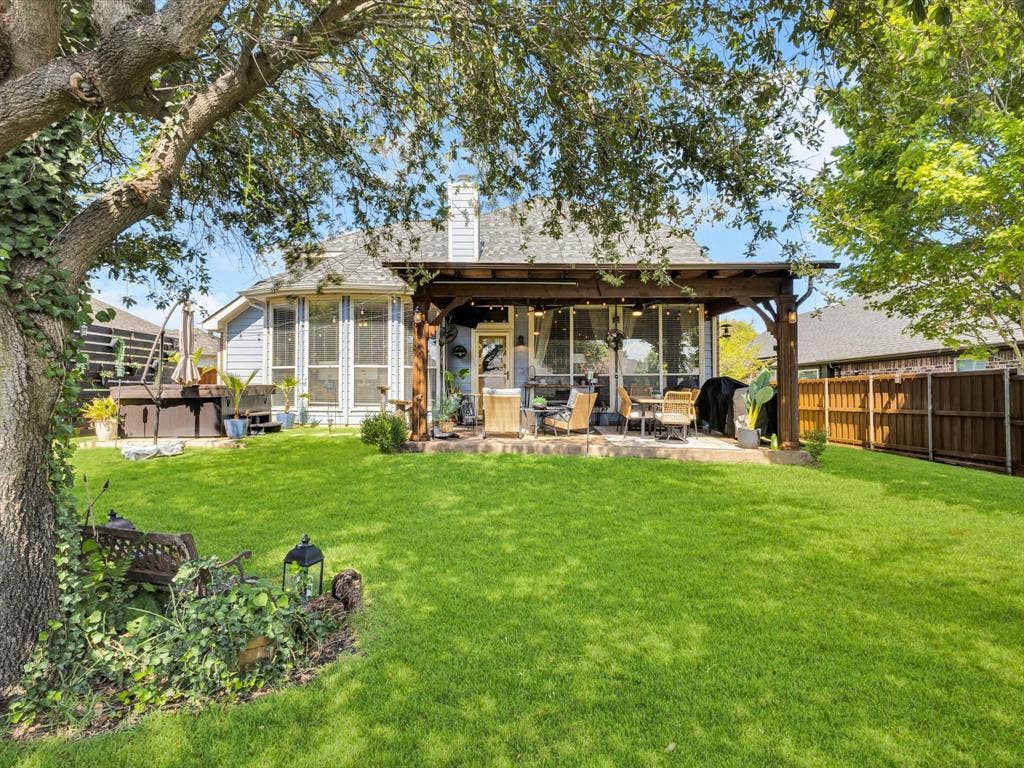 6004 Crestmill Lane, Sachse, TX 75048 Expansive backyard featuring a manicured lawn, mature trees, and a wooden pergola covering a patio area