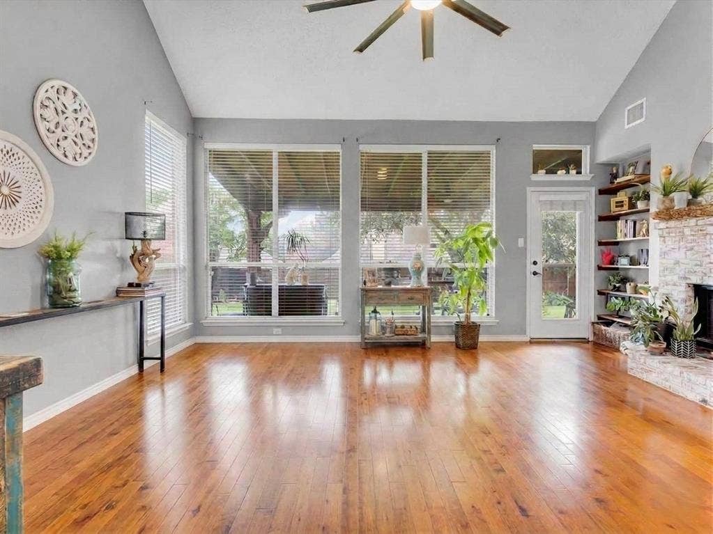 6004 Crestmill Lane, Sachse, TX 75048 Vaulted ceilings, wood-finish flooring, full-light glass door, built-in corner shelving, and a stone-clad fireplace