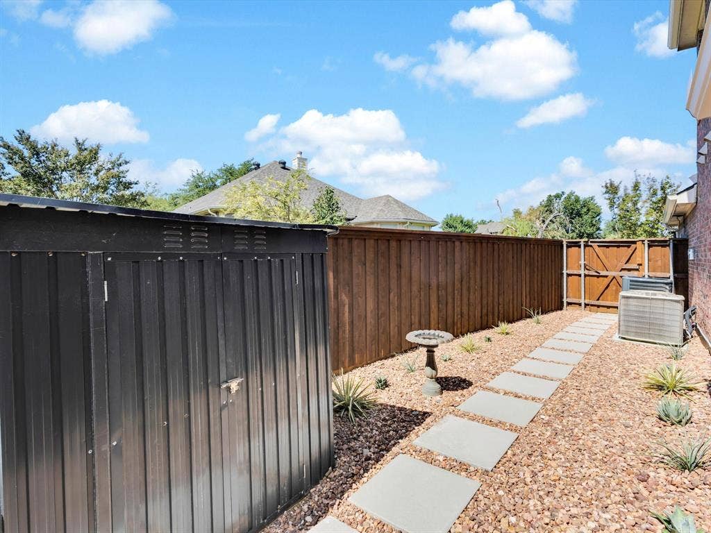 6004 Crestmill Lane, Sachse, TX 75048 Side yard featuring a dark metal storage shed, stepping stone pathway, and gravel landscaping
