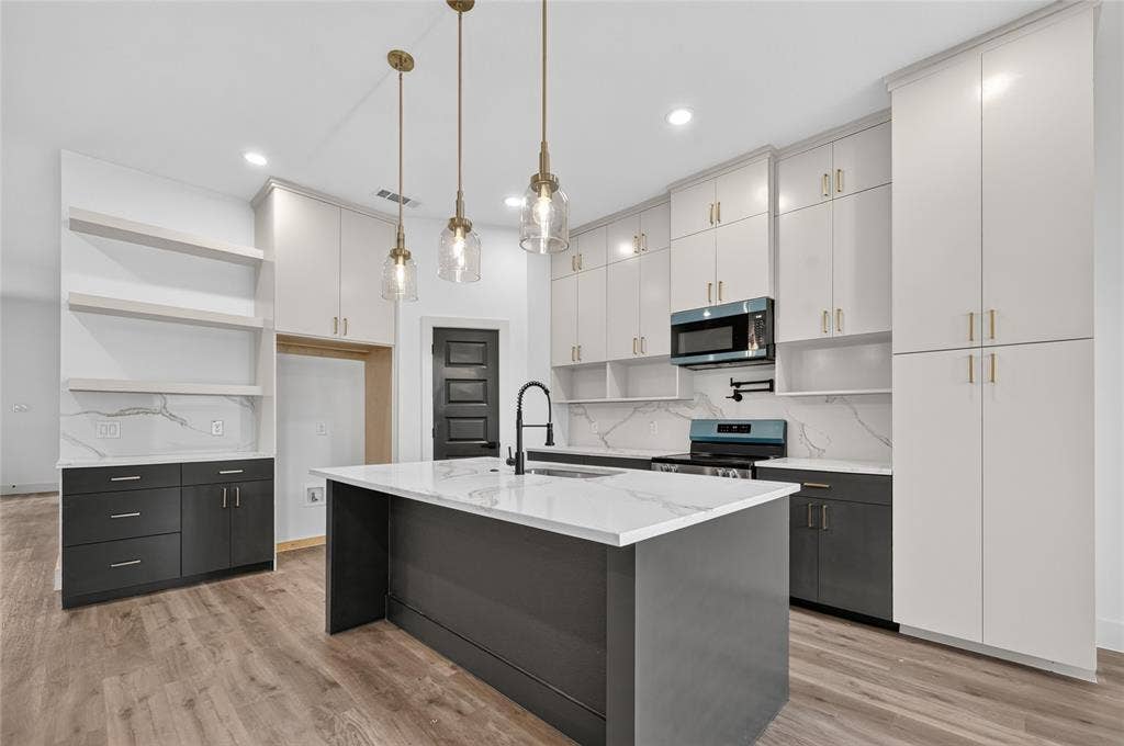 5130 Echo Avenue, Dallas, TX 75215 Modern kitchen featuring a central island with a waterfall countertop, contemporary pendant lighting, extensive white cabinetry, high-contrast dark lower cabinets, and wood-finish flooring