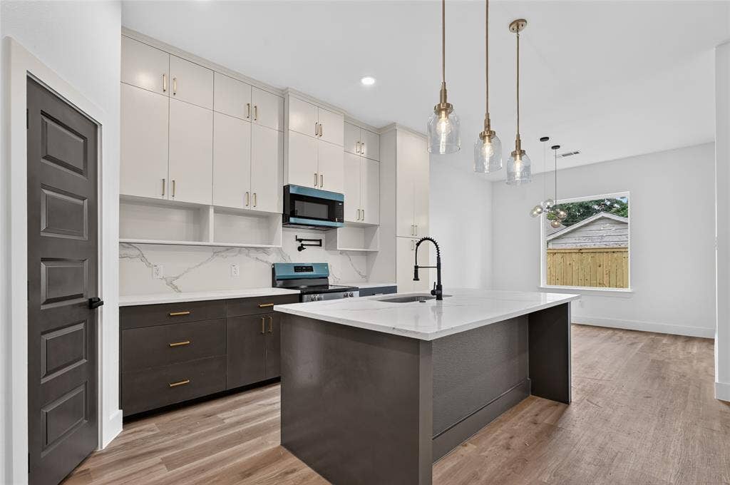 5130 Echo Avenue, Dallas, TX 75215 Modern kitchen featuring two-tone cabinetry with gold-tone hardware, a waterfall island with a gooseneck faucet, a patterned backsplash, and wood-finish flooring