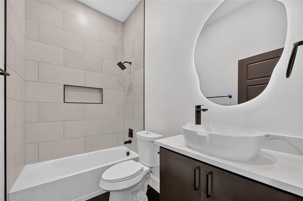 5130 Echo Avenue, Dallas, TX 75215 Bathroom featuring a vessel sink, dark wood-finish vanity with stone-look countertop, and an illuminated organic-shaped mirror
