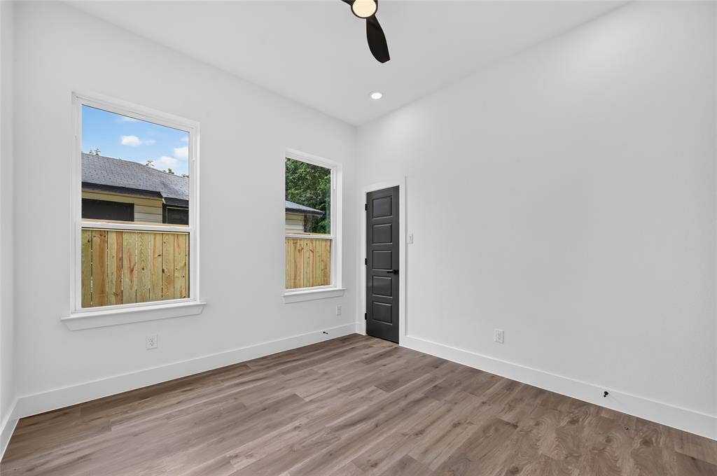 5130 Echo Avenue, Dallas, TX 75215 Spacious room featuring wood-finish flooring, two large windows, a ceiling fan, recessed lighting, and a modern dark panel door