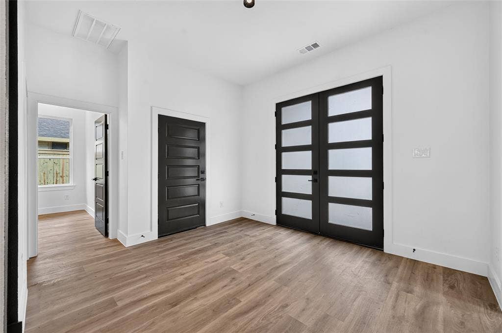 5130 Echo Avenue, Dallas, TX 75215 Spacious room featuring wood-finish flooring, white walls, and a pair of modern French doors with frosted glass panels