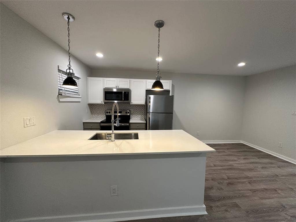 5018 San Jacinto Street, #107, Dallas, TX 75206 Kitchen featuring a central island with an undermount sink, pendant lighting, white upper cabinetry, stainless steel appliances, and wood-finish flooring