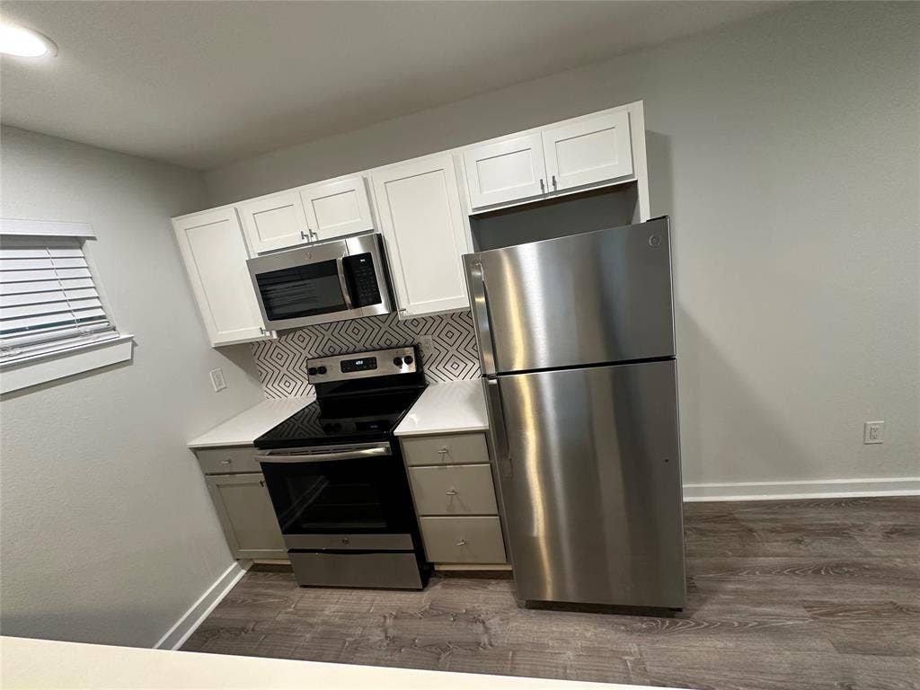 5018 San Jacinto Street, #107, Dallas, TX 75206 Kitchen featuring stainless steel appliances, white upper cabinetry, gray lower cabinetry, a patterned tile backsplash, and wood-finish flooring