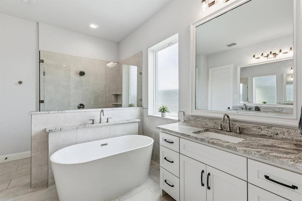 Contemporary bathroom featuring a freestanding soaking tub, a large walk-in shower with glass enclosure, a white double vanity with stone countertops, and a frosted window