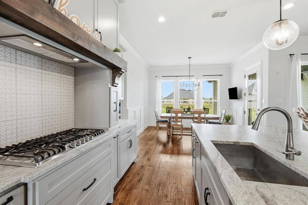 Gourmet kitchen featuring a built-in gas range with decorative hood, light gray cabinetry, and granite countertops