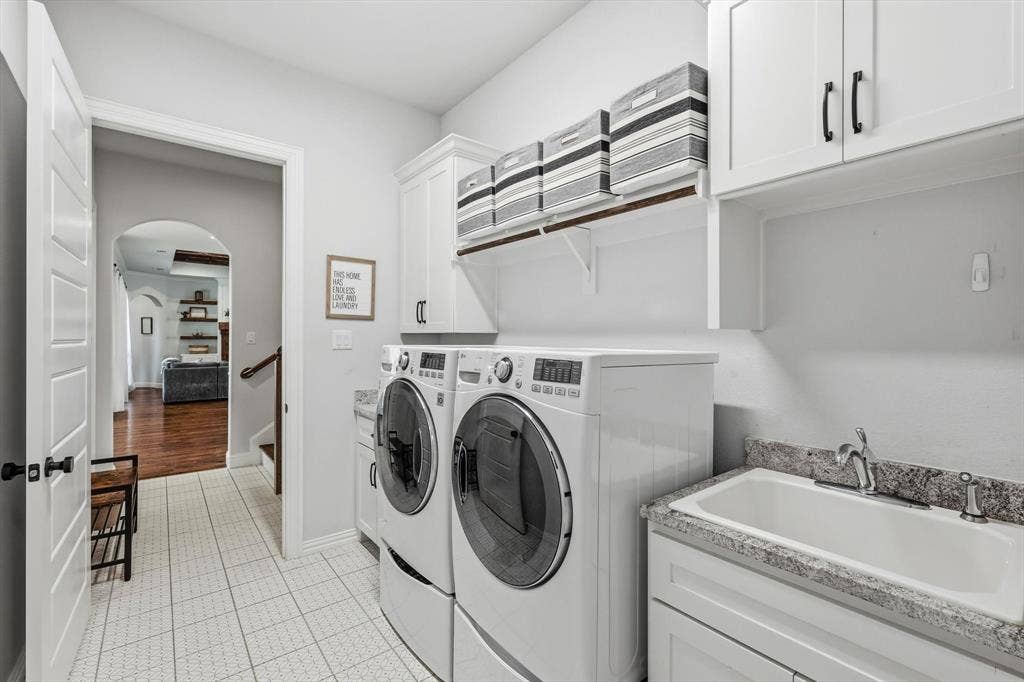 Dedicated laundry room with direct access to Primary bedroom featuring white shaker-style cabinetry, a utility sink with a stone-finish countertop, and white tile flooring