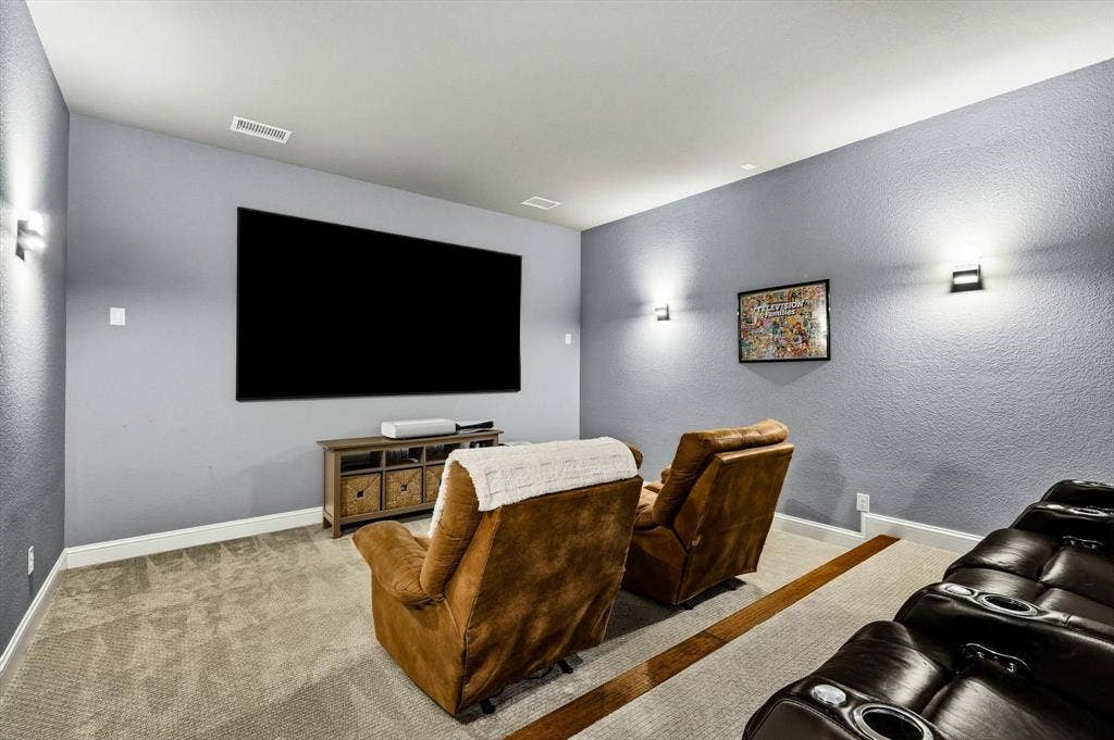 Downstairs dedicated media room featuring a large screen, light gray walls, and recessed ceiling vents