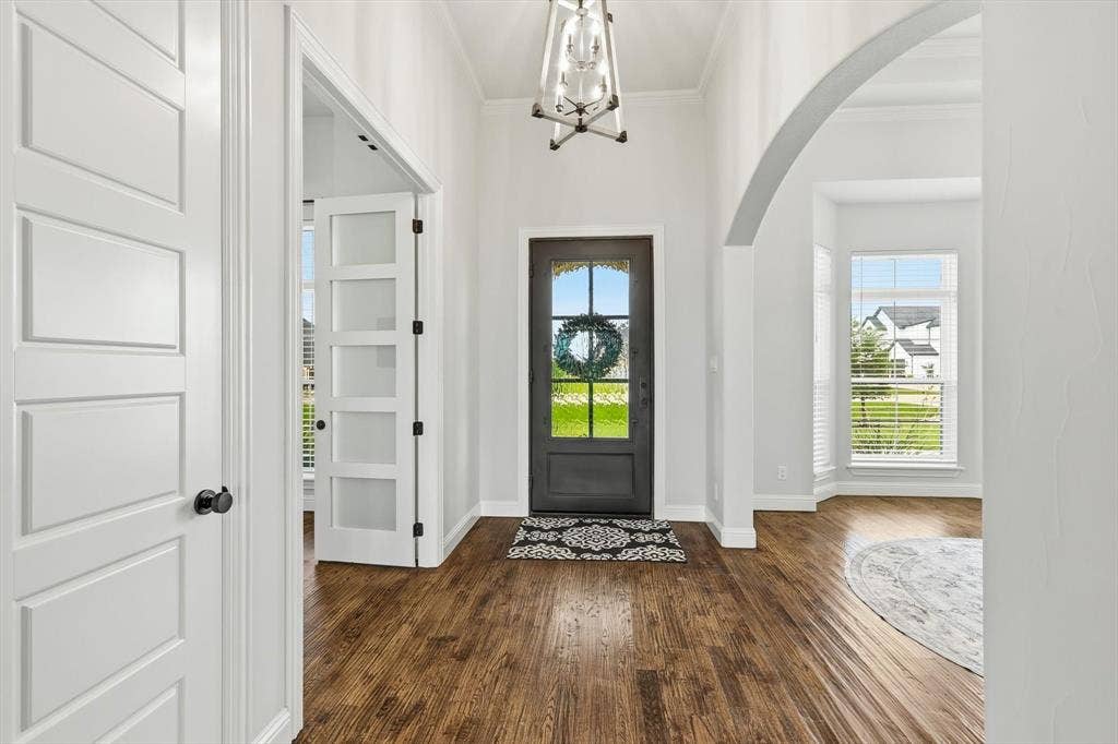 Entryway featuring wood-finish flooring, a contemporary overhead light fixture, and a dark-paneled front door with arched glass