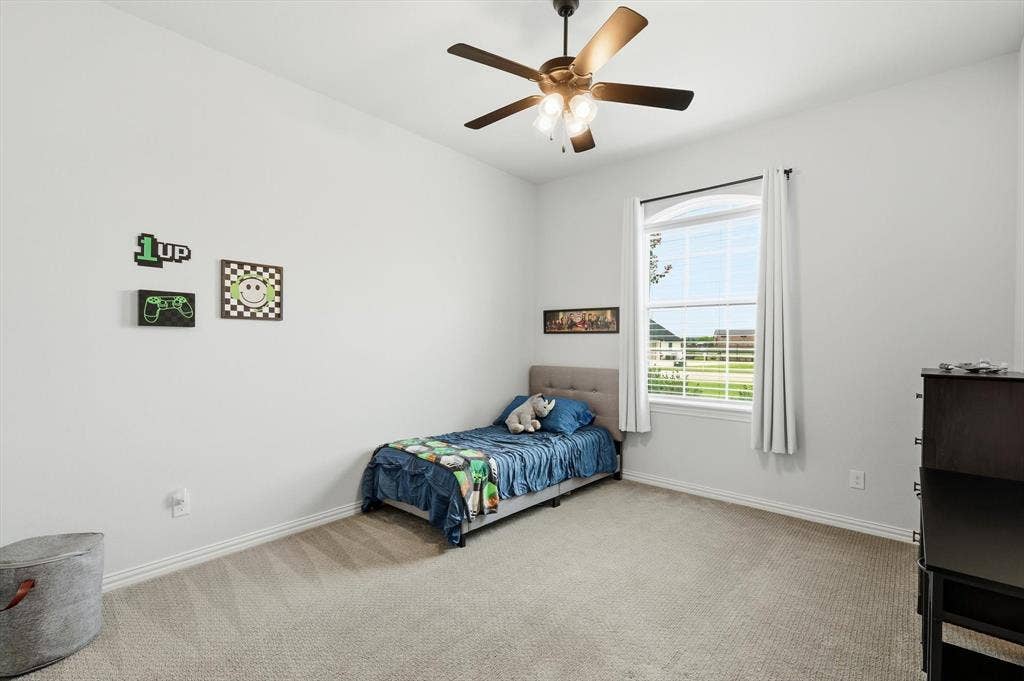 Spacious room featuring neutral carpeting, a large window with blinds, and an overhead ceiling fan with integrated lighting