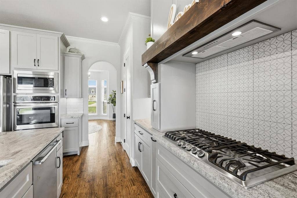 Kitchen featuring a stainless steel gas range, patterned tile backsplash, and light-toned cabinetry