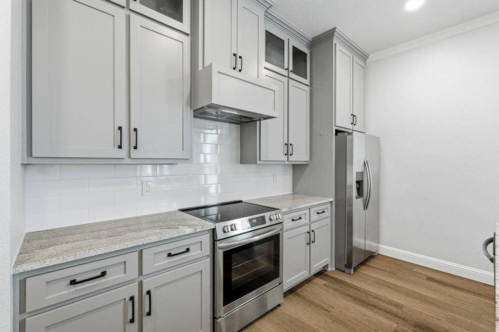 Guest Home - Kitchen featuring light gray shaker cabinetry, stainless steel appliances, a white subway tile backsplash, and light-toned countertops