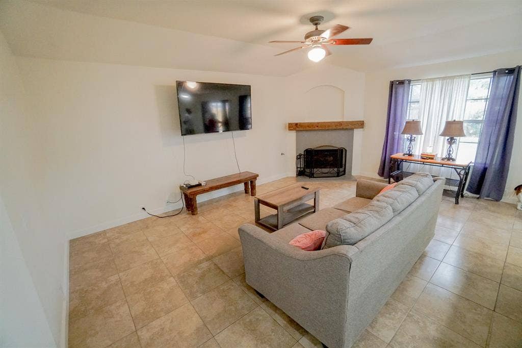 203 Grassy Creek Drive, Wylie, TX 75098 Bright interior space featuring a ceiling fan with integrated lighting, a fireplace with a wood mantel, tiled flooring, and multiple windows