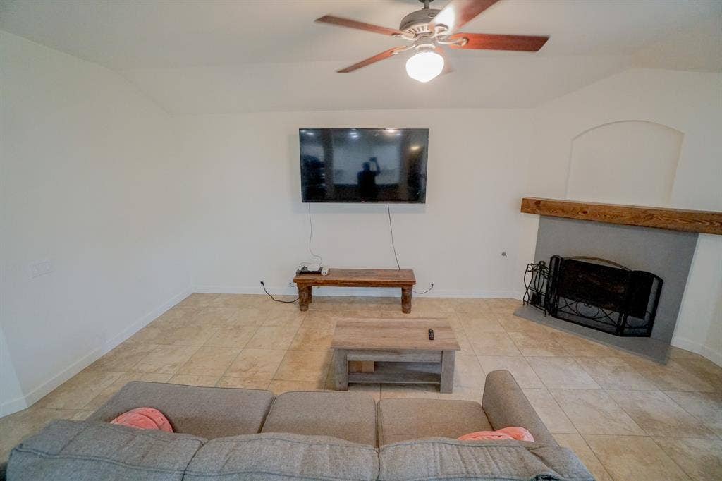 203 Grassy Creek Drive, Wylie, TX 75098 Spacious living area featuring tile flooring, a ceiling fan with integrated lighting, and an arched fireplace with a substantial wood mantel