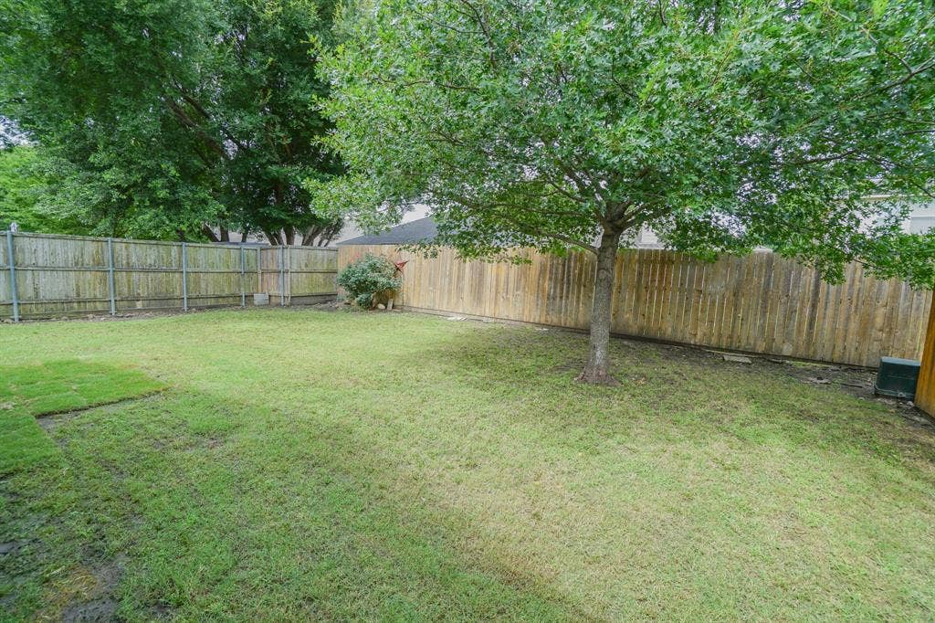 203 Grassy Creek Drive, Wylie, TX 75098 Expansive backyard featuring a mature tree, perimeter wood fencing, and a partial section of newly laid sod