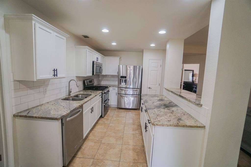 203 Grassy Creek Drive, Wylie, TX 75098 Kitchen featuring white cabinetry with dark hardware, stone countertops, a tile backsplash, and stainless steel appliances. 203 Grassy Creek Dr, Wylie, TX 75098