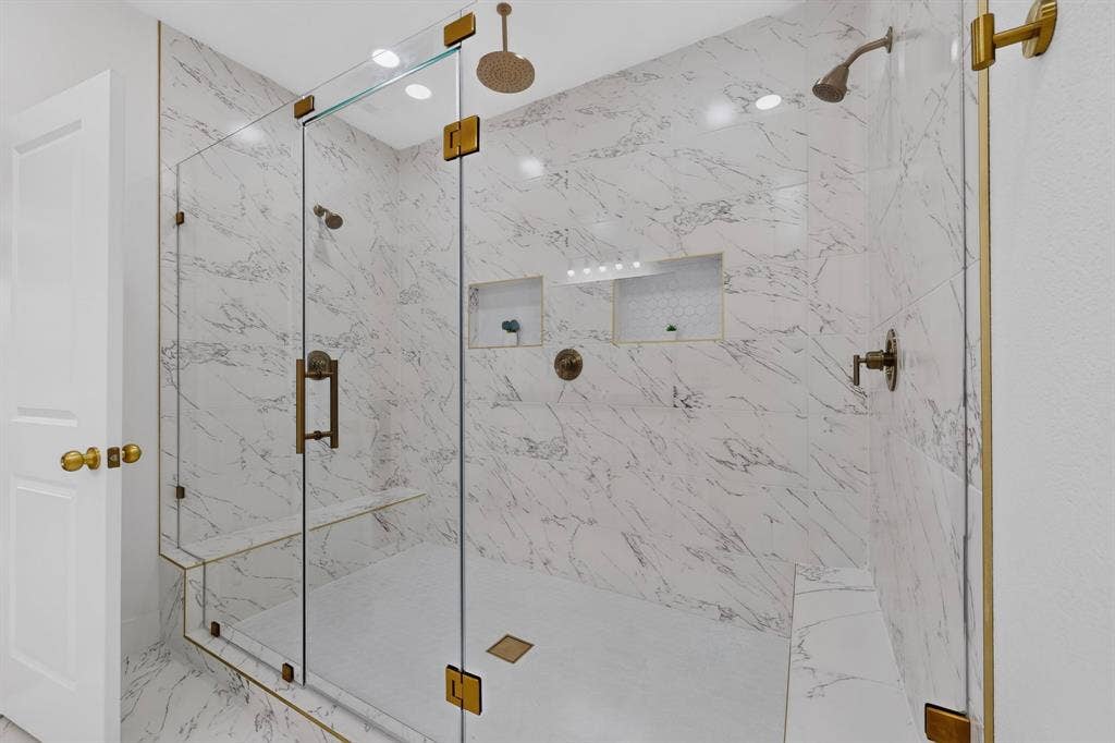 343 SCHOONER Road, Gun Barrel City, TX 75156 Spacious glass-enclosed shower featuring large format marble-look tile, dual shower heads, integrated bench seating, recessed niches, and brass-finish hardware