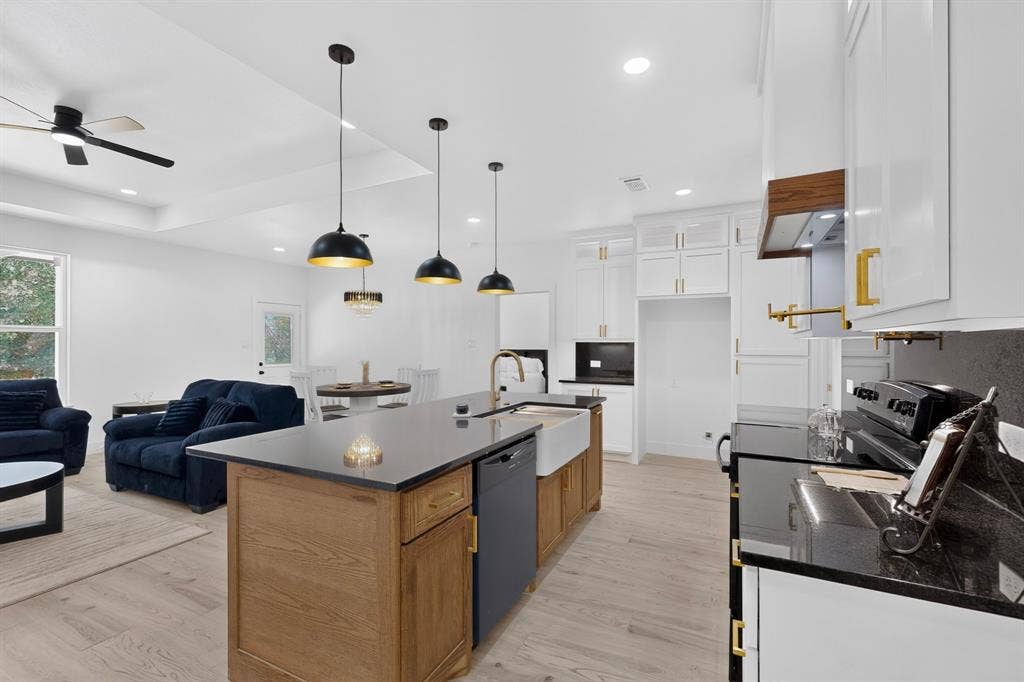343 SCHOONER Road, Gun Barrel City, TX 75156 Open-concept kitchen featuring an oversized island with a farmhouse sink, black granite-style countertops, white cabinetry with gold-tone hardware, and light wood-finish flooring