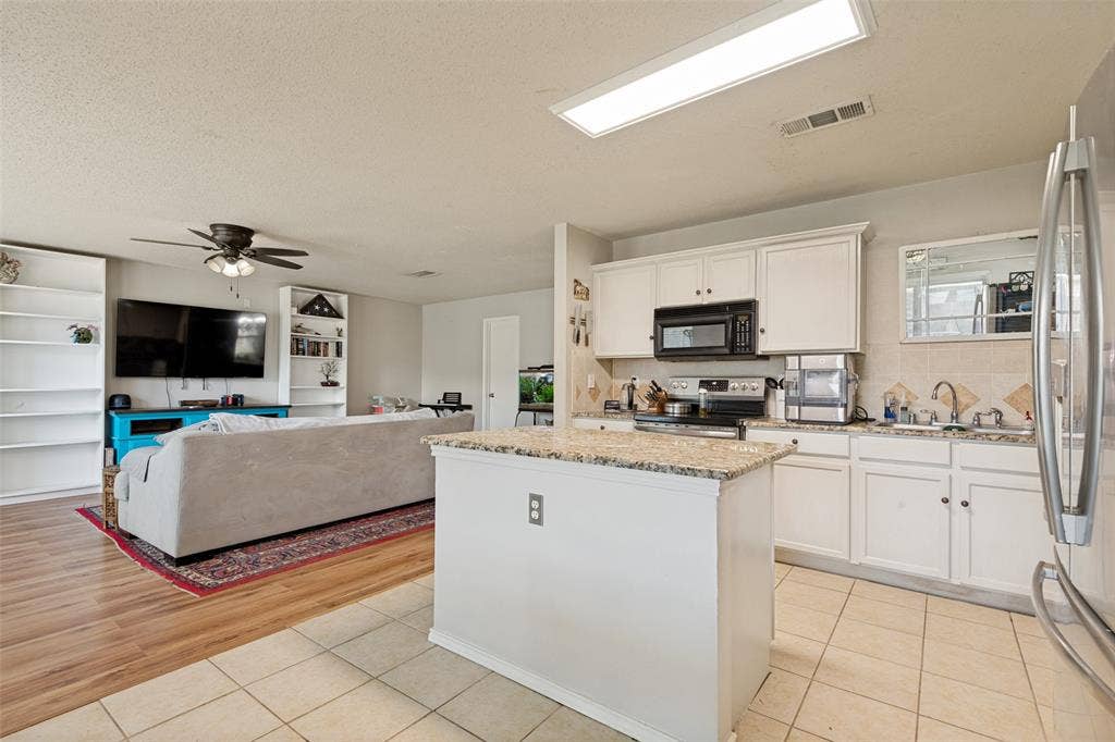 605 Rock Brook Drive, Forney, TX 75126 Open-concept kitchen and living area featuring a central kitchen island with a stone-finish countertop, white cabinetry, a stainless steel refrigerator, and tiled flooring