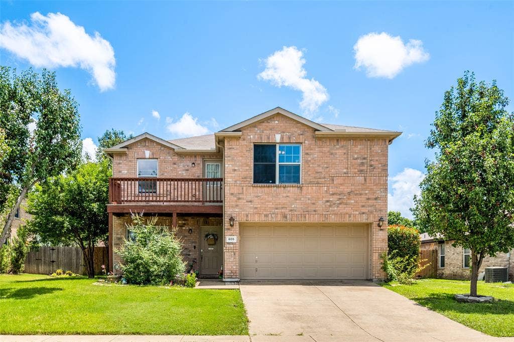 605 Rock Brook Drive, Forney, TX 75126 Two-story brick exterior featuring a second-level balcony with wood railing, a two-car garage, and a concrete driveway