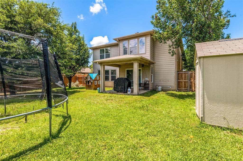605 Rock Brook Drive, Forney, TX 75126 Expansive grassy backyard featuring a covered patio, a detached storage shed, mature trees, and privacy fencing