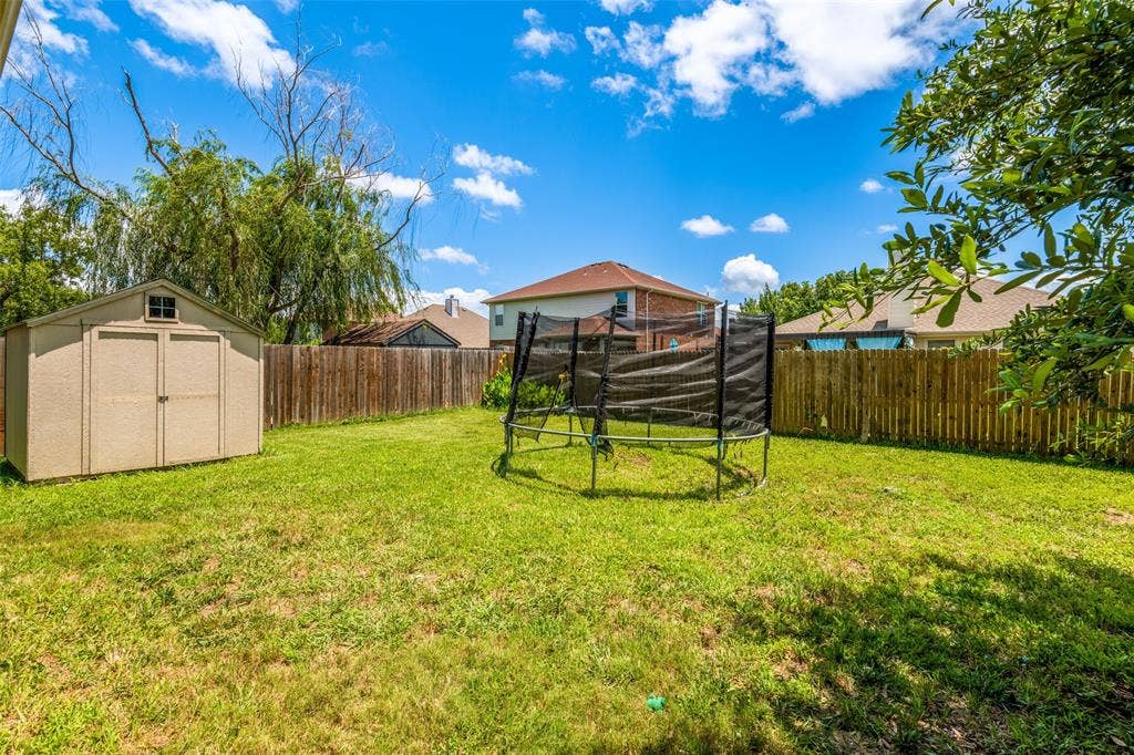 605 Rock Brook Drive, Forney, TX 75126 Expansive backyard featuring a manicured lawn, a detached storage shed, and a privacy fence