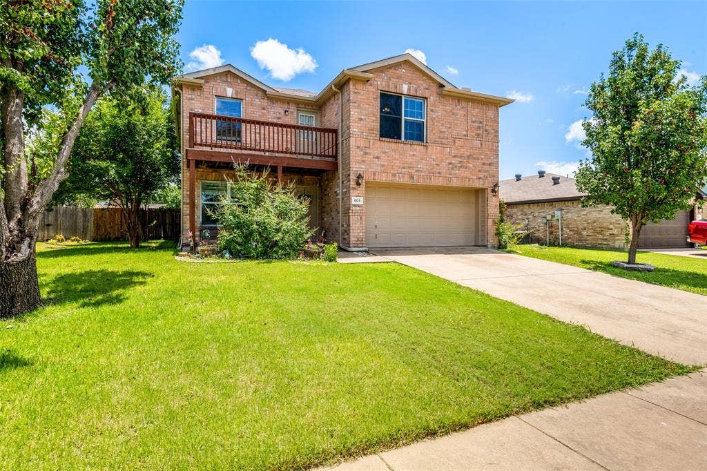 605 Rock Brook Drive, Forney, TX 75126 Brick exterior residence featuring a second-story balcony with wood railing, an attached garage, and a concrete driveway