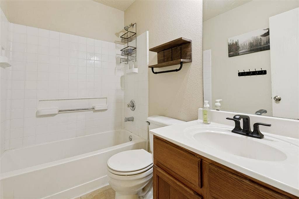 605 Rock Brook Drive, Forney, TX 75126 Full bathroom featuring a white ceramic bathtub with tiled surround, a white toilet, and a vanity with a white countertop and wood-finish cabinetry