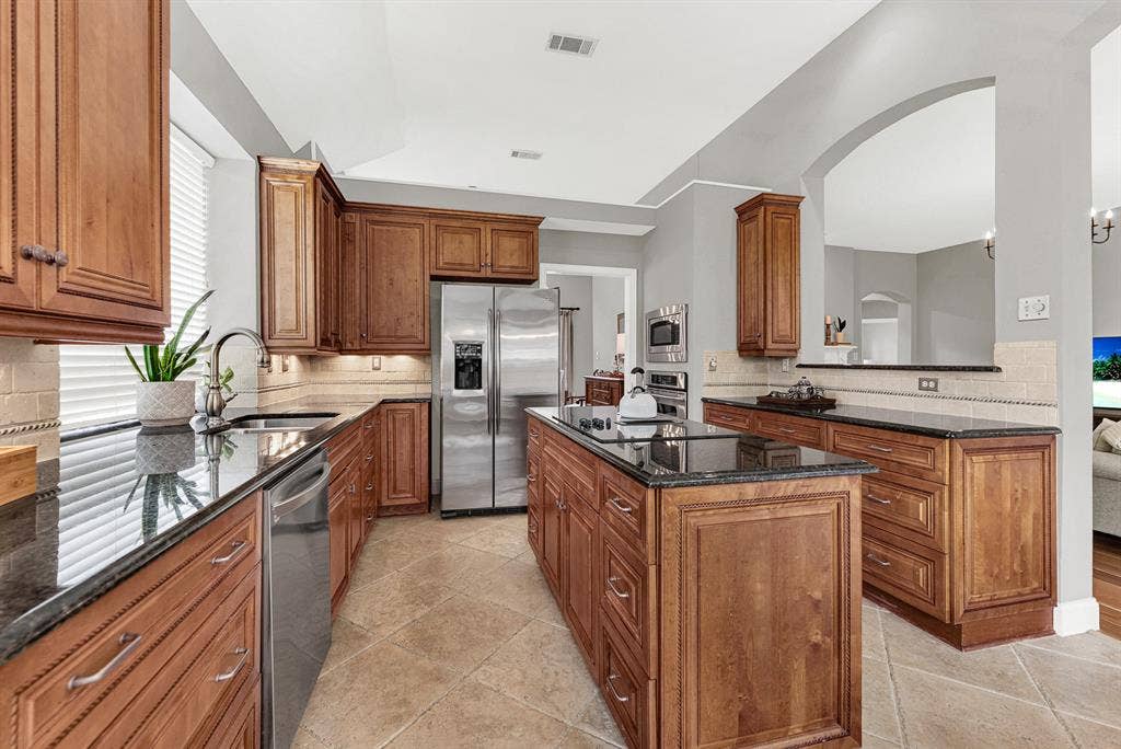 3708 Stockport Drive, Plano, TX 75025 The kitchen opens through a graceful arch into the family room beyond, keeping the cook connected to the rest of the home while the vaulted ceiling above adds unexpected volume. Weeknight dinners feel easy here — the layout was made for people who actually cook.