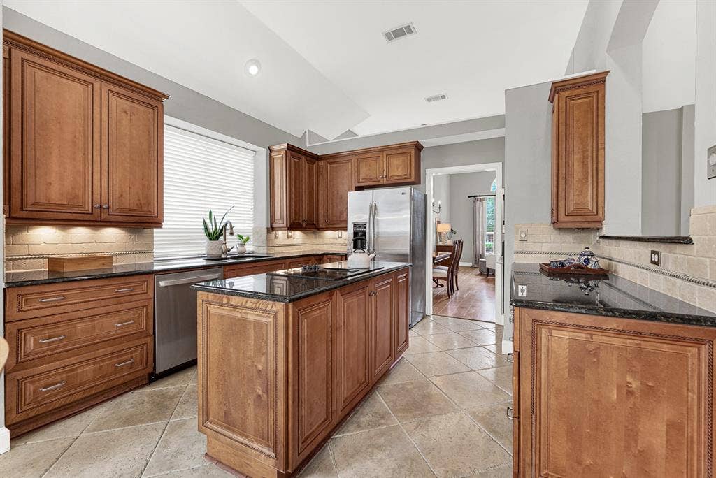 3708 Stockport Drive, Plano, TX 75025 Under-cabinet lighting glows warmly across the rope-detailed custom cabinetry and travertine backsplash, while large-format tile floors anchor the space with quiet elegance. This is a kitchen that rewards the cook — every inch of counter and cabinet space was thought through carefully.